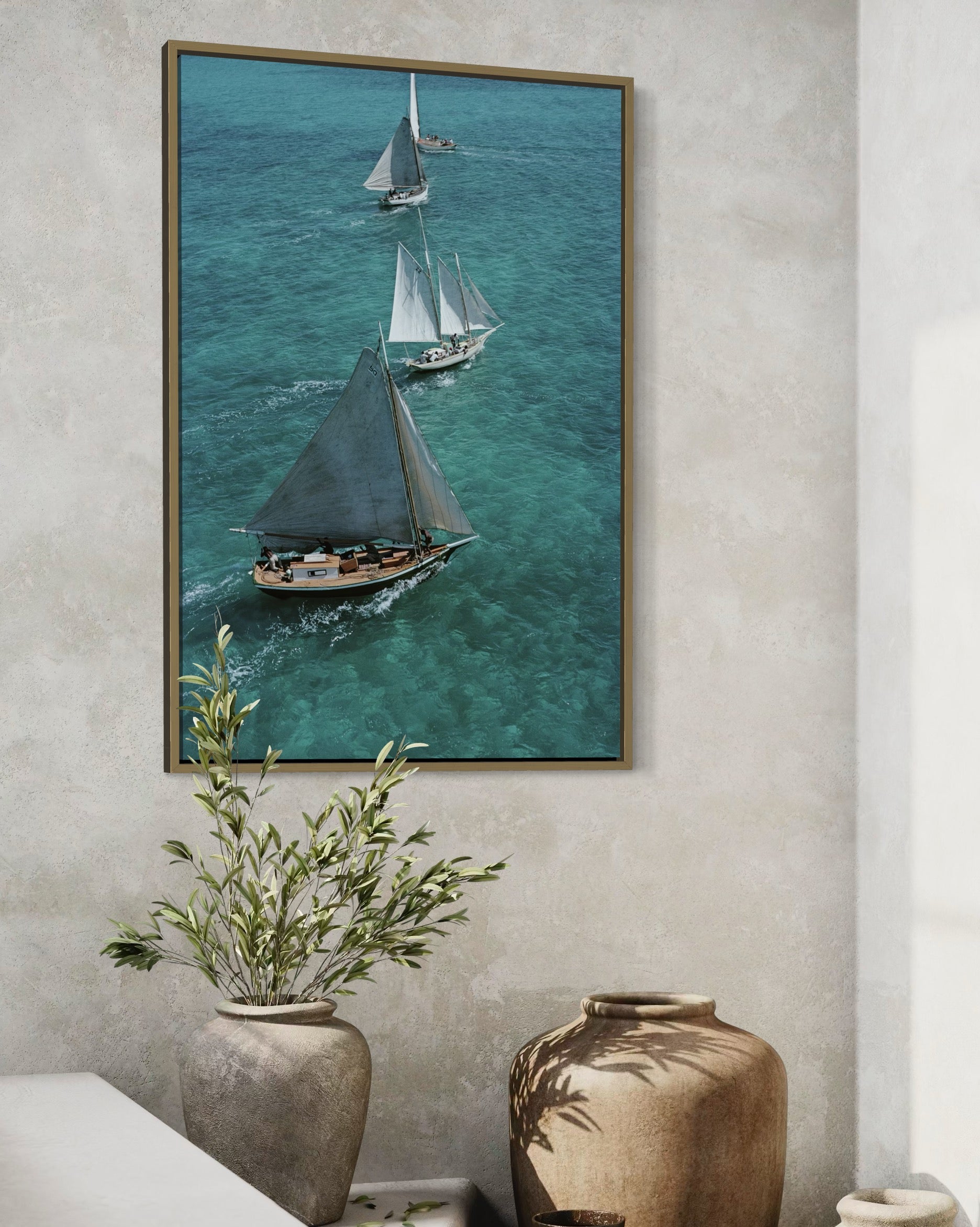 Framed artwork of sailboats on a blue ocean wall-mounted above a decorative plant and vase.