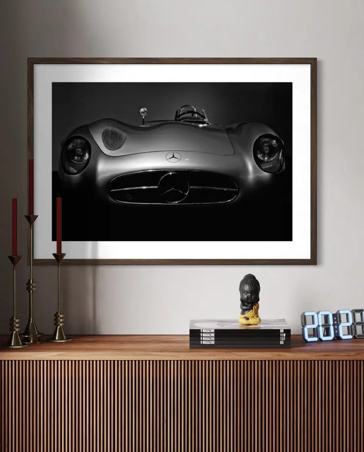 A framed black and white art print of a Mercedes-Benz 300 SL Roadster car, displayed on a light gray wall above a wooden console table with decorative items.