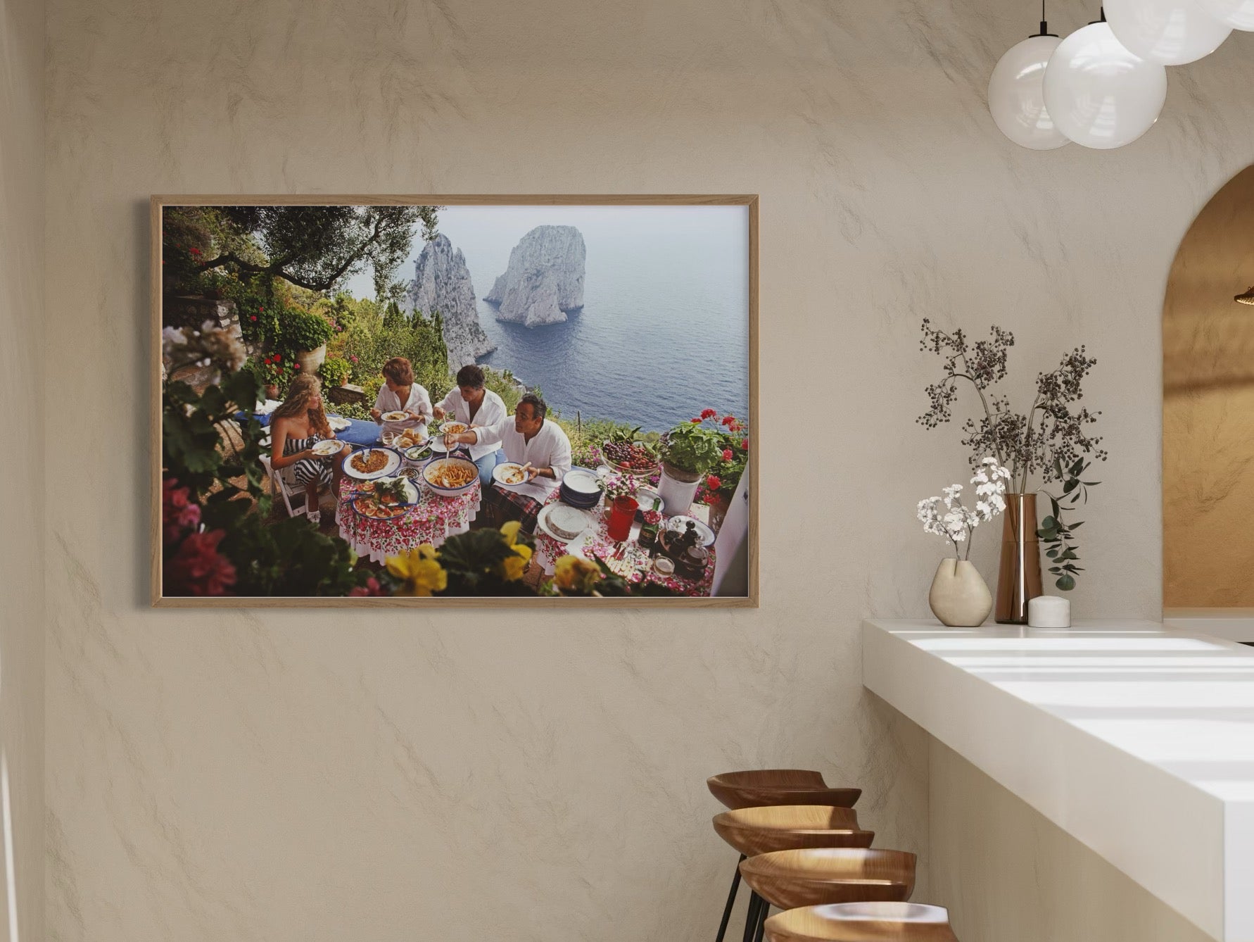 Framed artwork of a scenic coastal scene with people dining, displayed on a wall.
