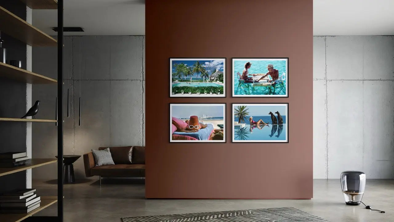 A set of four framed tropical beach and poolside photographs displayed in a 2x2 grid on a terracotta-colored wall in a modern, minimalist living room.