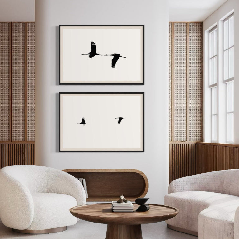 Modern living room with white chairs, a wooden table, and framed black and white artwork on the wall.