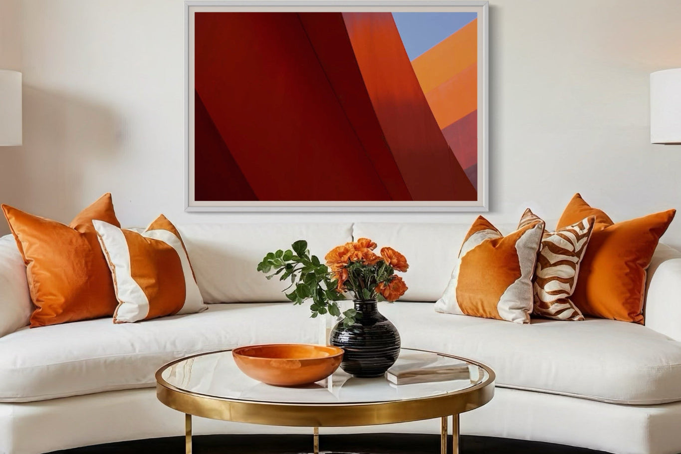 Modern living room with a white sofa, orange and white pillows, a gold coffee table, and abstract art on the wall.
