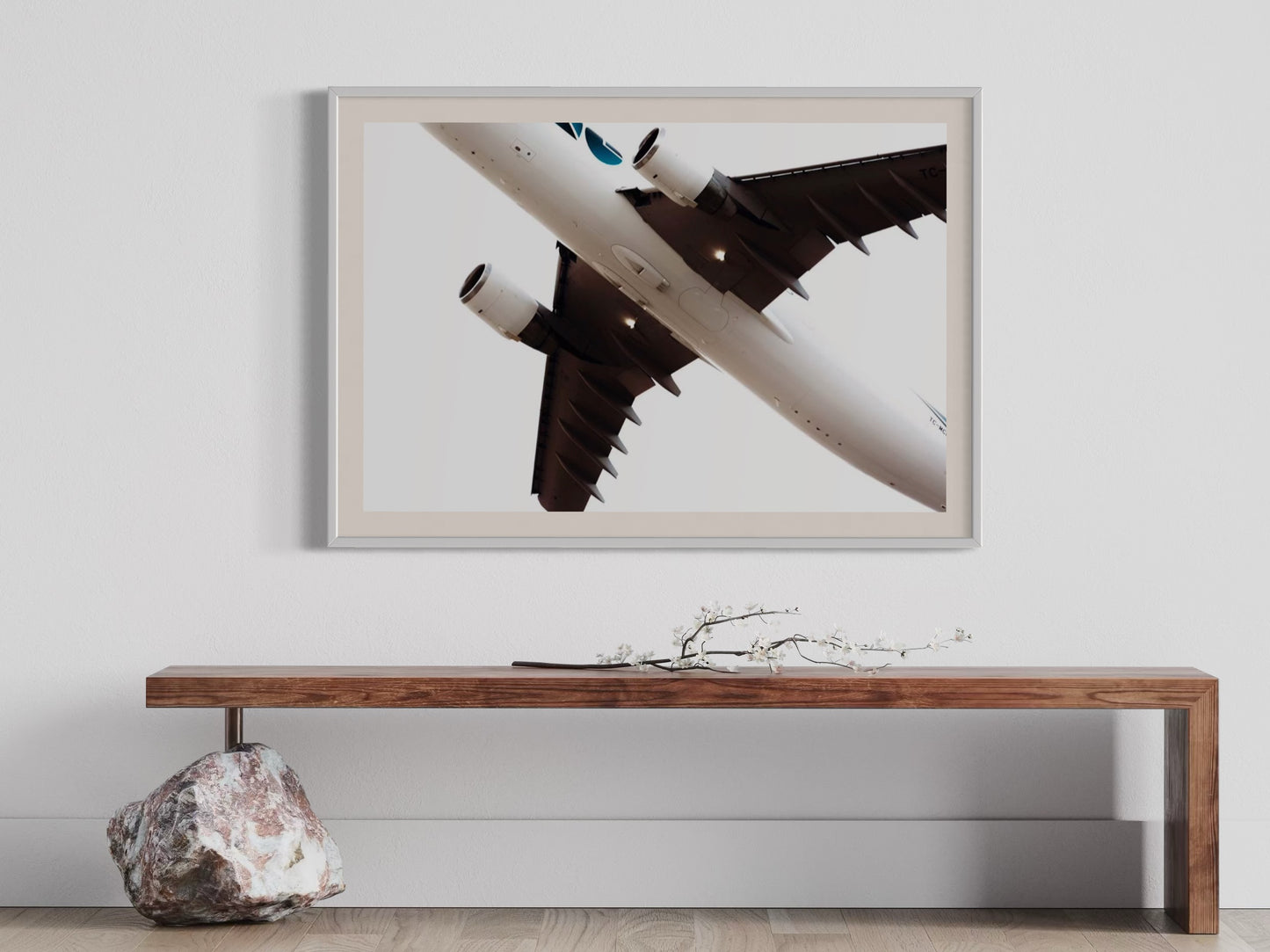 Framed artwork of an airplane on a white wall above a wooden bench.