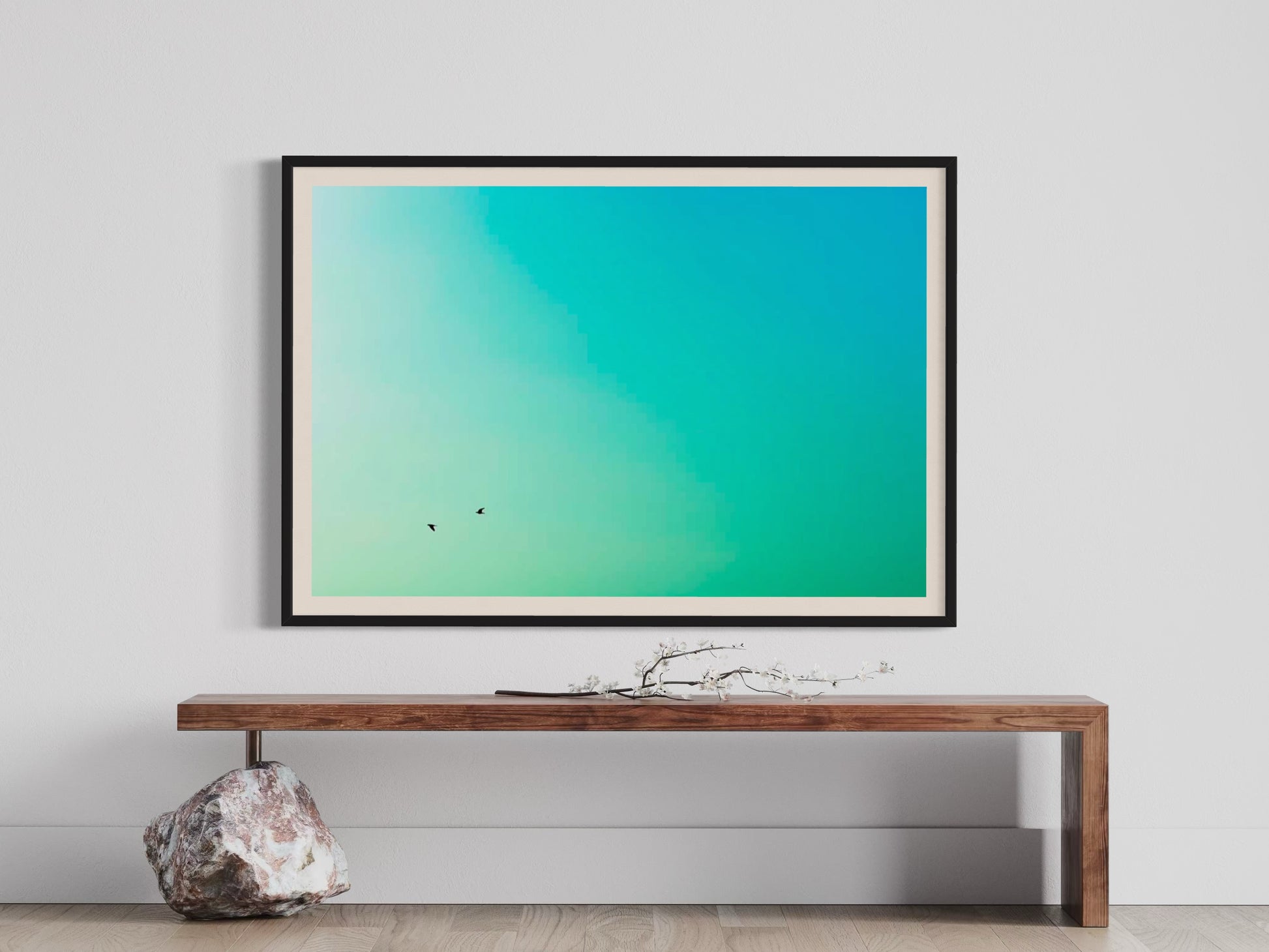 Framed artwork with a gradient of blue and green on a white wall above a wooden console table.