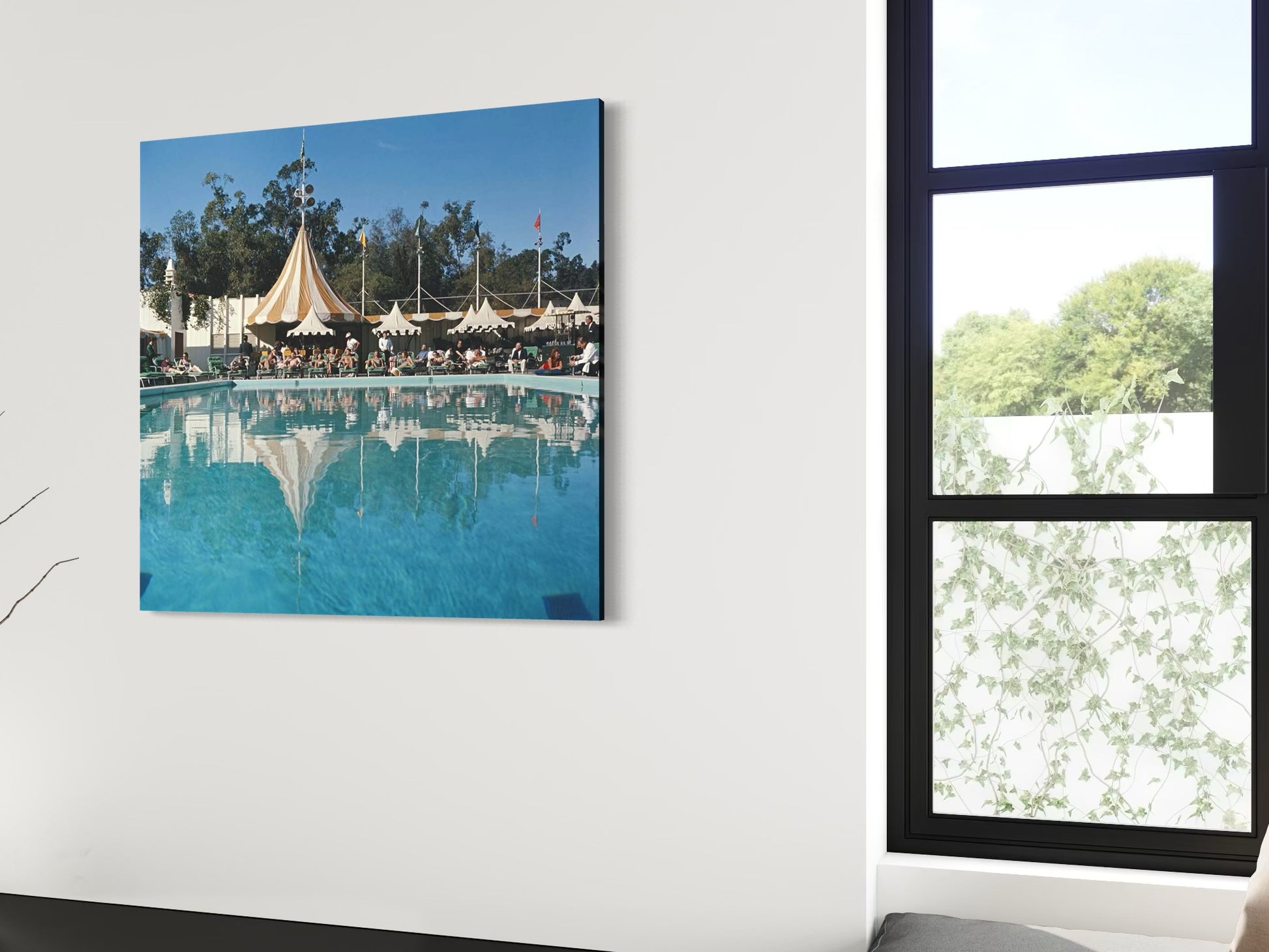 Unframed metal print of a pool scene with tents on a white wall next to a window.