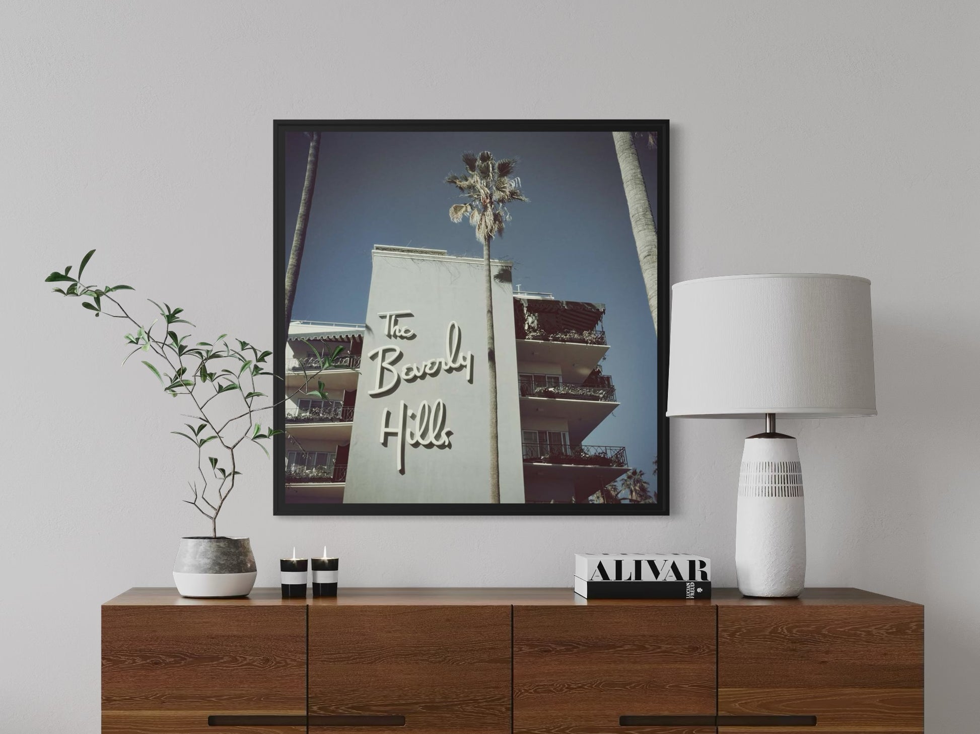 Framed artwork of a building with 'The Beach' sign on a wall above a wooden cabinet.