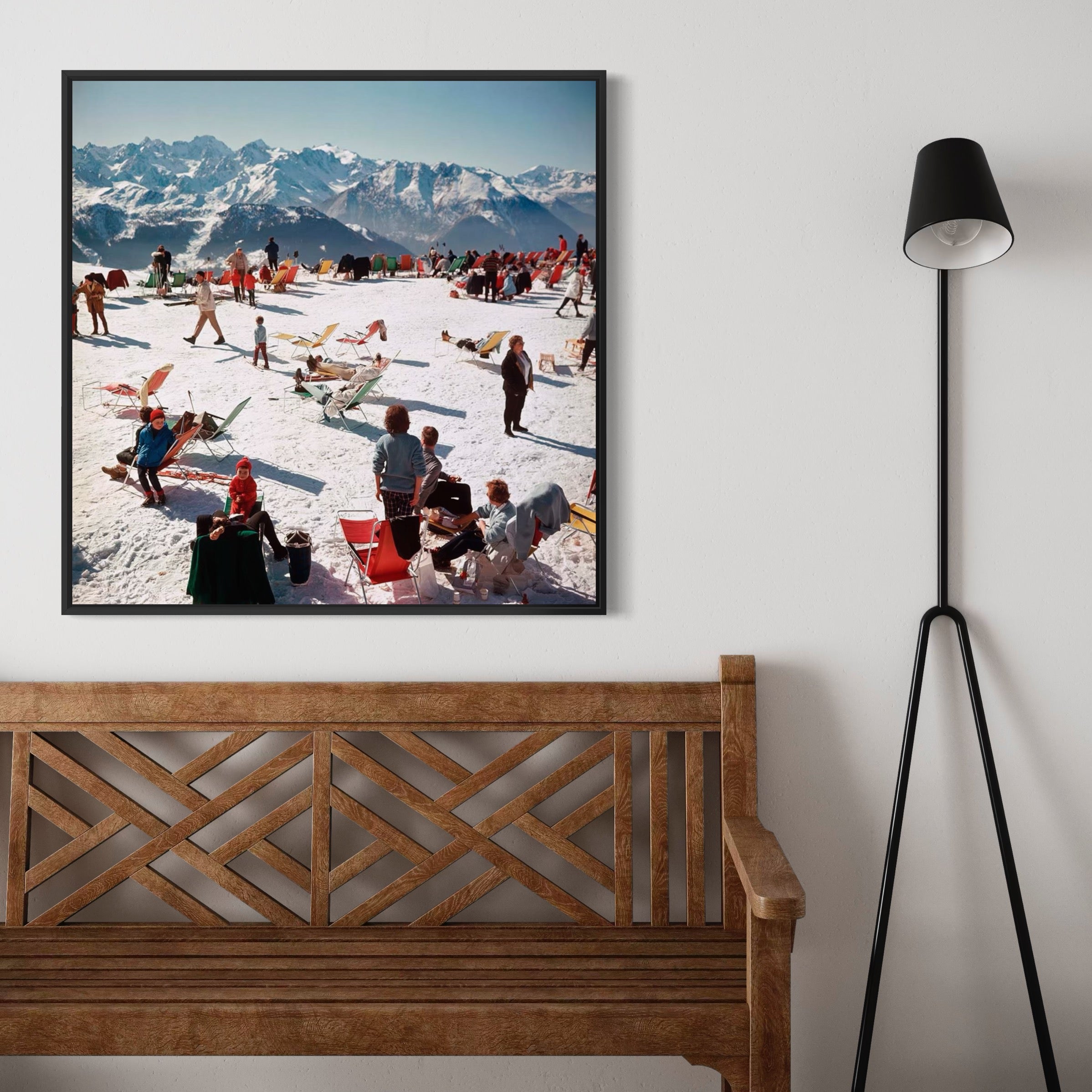 Framed photograph of a snowy mountain scene with people on a wall above a wooden bench.