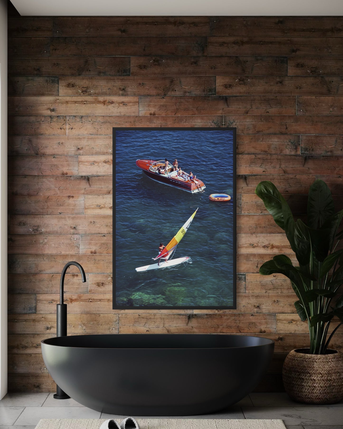 Framed artwork of a boat and paddleboard on a wooden wall above a black freestanding bathtub.