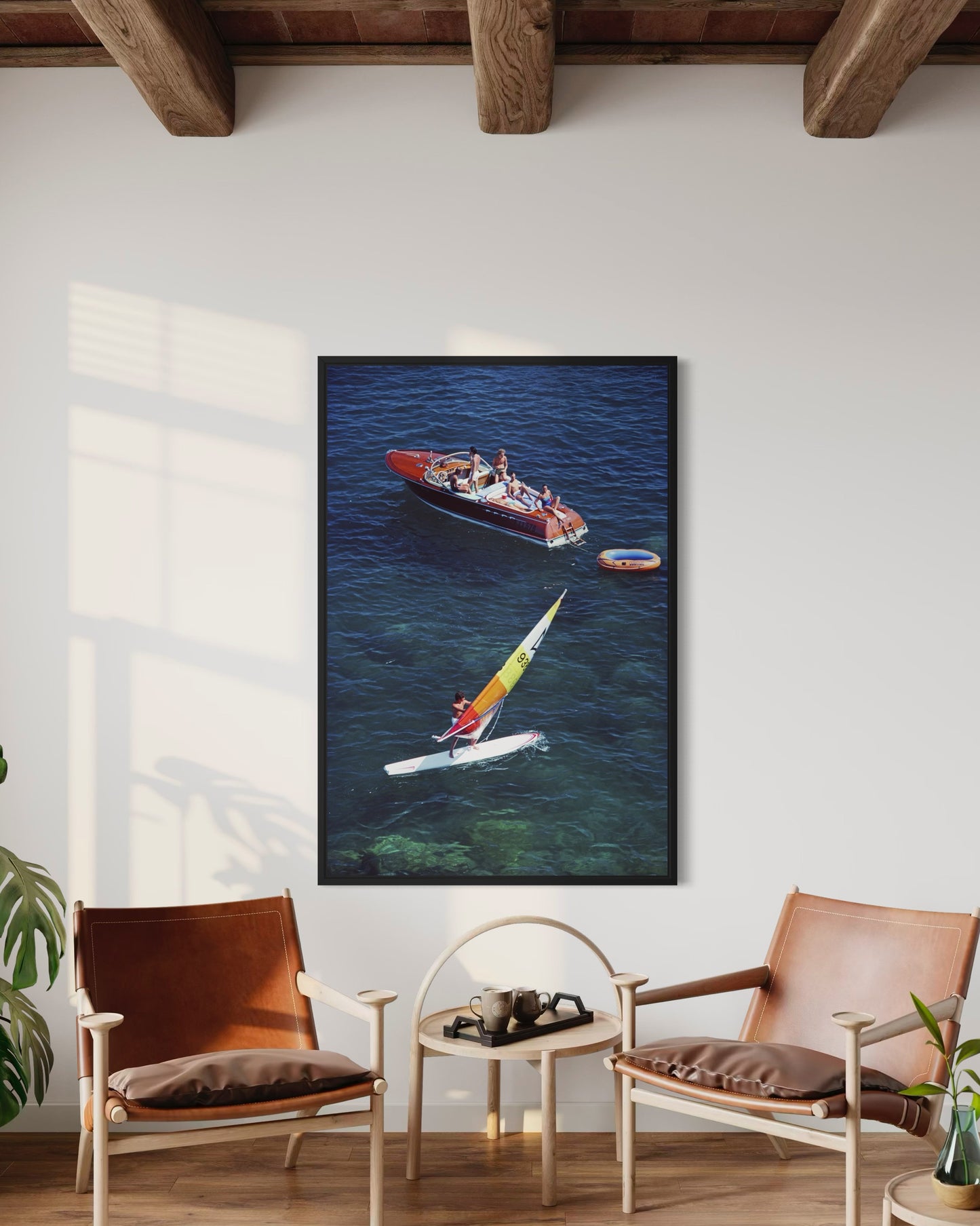 Framed artwork of a boat and kayaker on a wall in a room with chairs and a table.