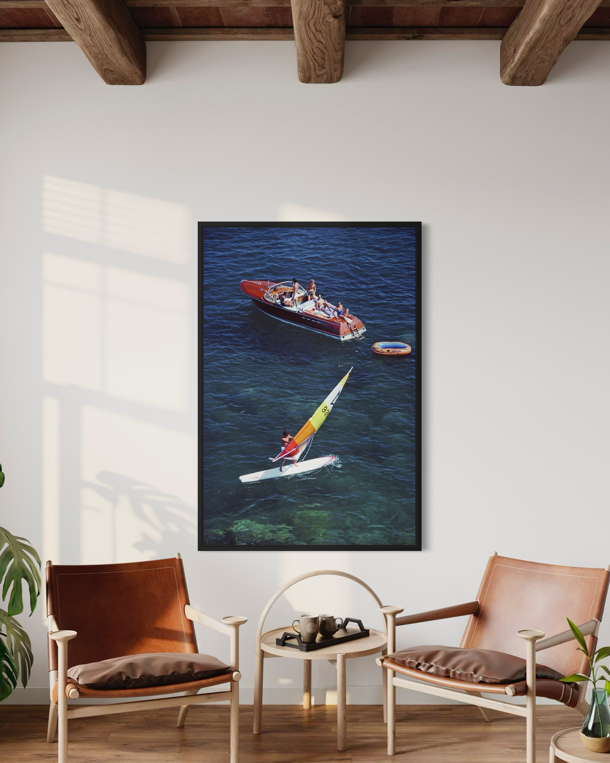 Framed artwork of a boat and kayaker on a wall in a room with chairs and a table.