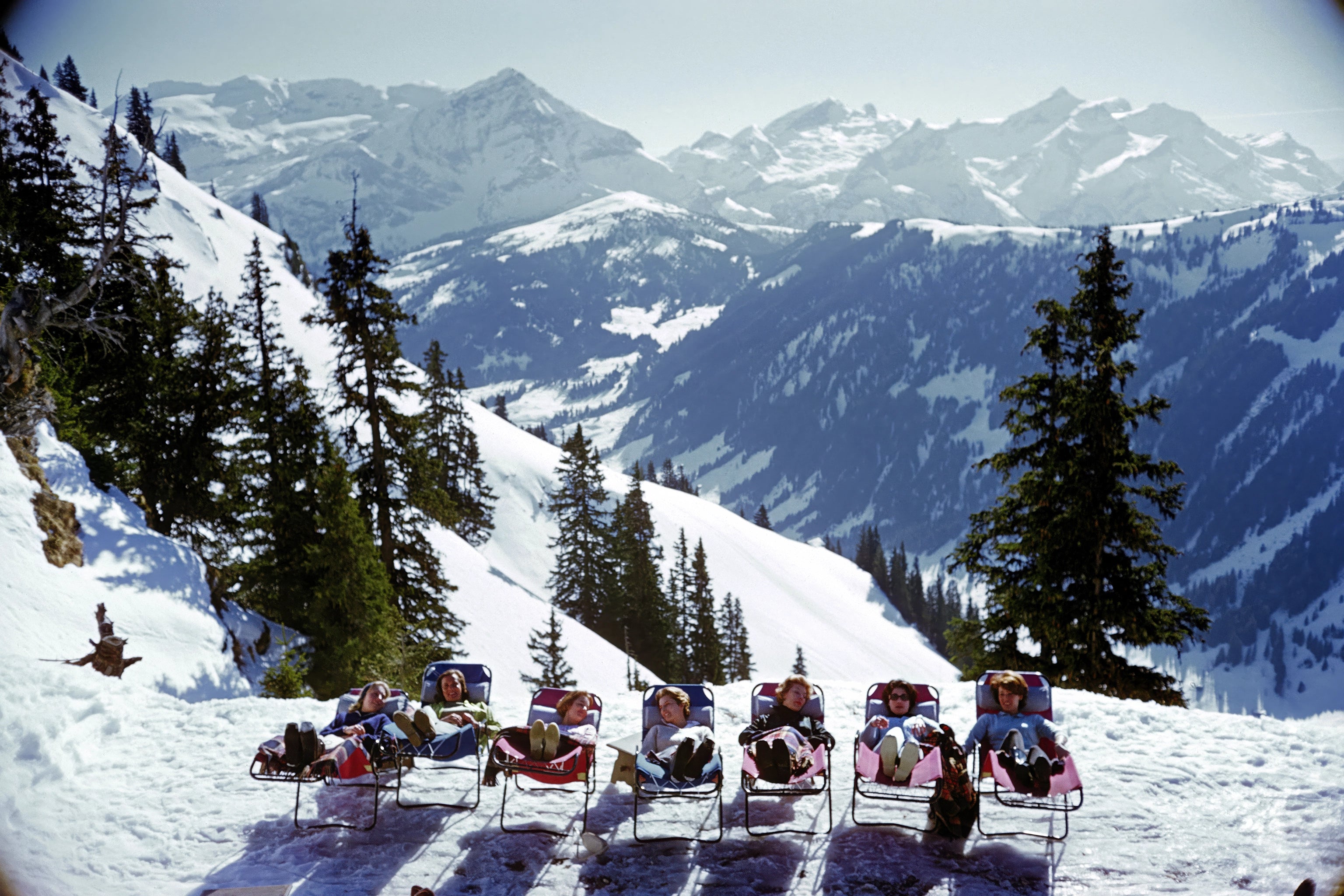 People sitting in chairs on a snowy slope in Gstaad with mountains of the Swiss Alps in the background