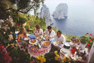 Group of people dining outdoors with scenic ocean view and rocky cliffs.