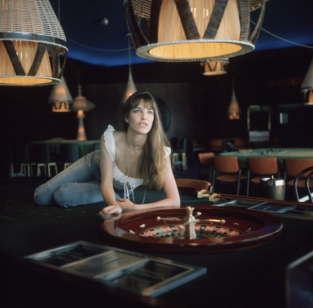 A black and white photo of an actress lying on a roulette table, with a white paper border around the image.