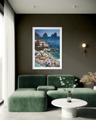 A framed art print of a colorful coastal village and harbor scene with boats and blue water, displayed on a dark wall above a green sectional sofa in a modern living room.