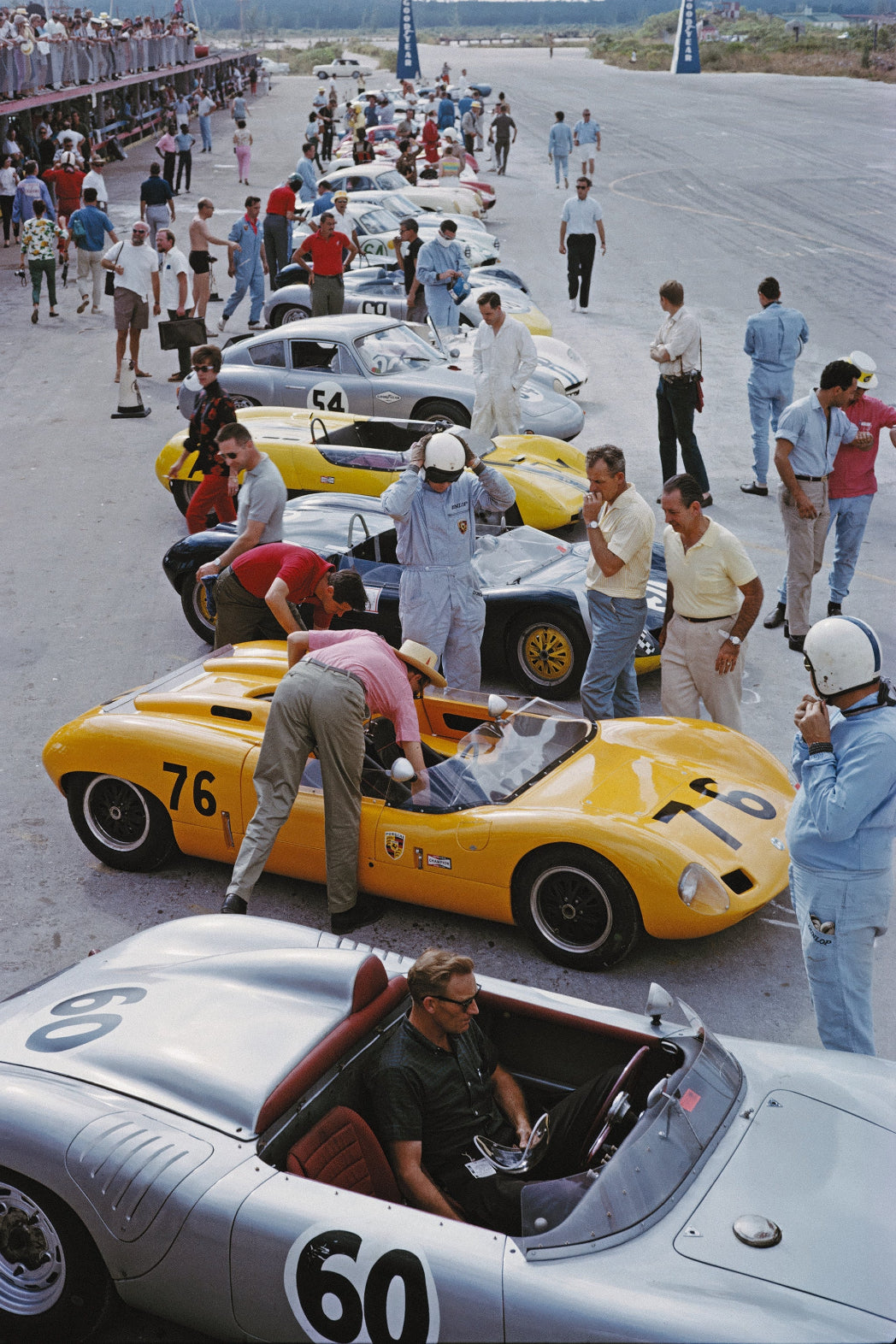 Vintage race cars on a track with mechanics and spectators, photographed by Slim Aarons