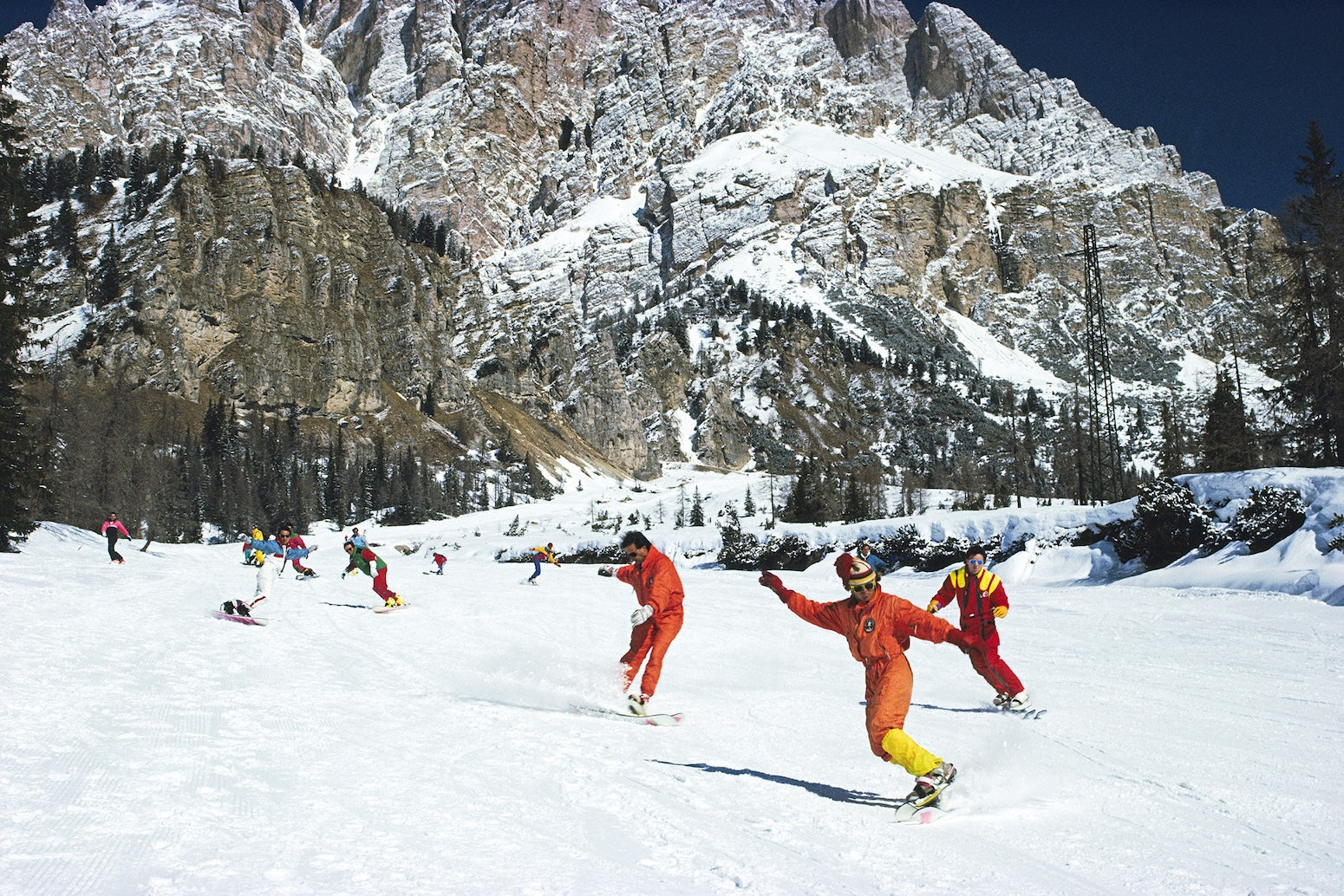 People skiing on a snowy mountain with snow-covered trees and mountains in the background.  The Picturalist Slim Aarons Collection