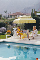 Three women sitting by a pool with a yellow umbrella and poolside decor. The Picturalist Wall Art and Photography for Designed Interiors. Slim Aarons Collection, Poolside. Getty Images Gallery.