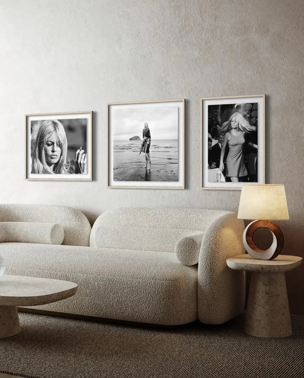 Three framed black and white portrait and beach photographs hang on a textured light gray wall above a cream boucle sofa in a modern living room setting.