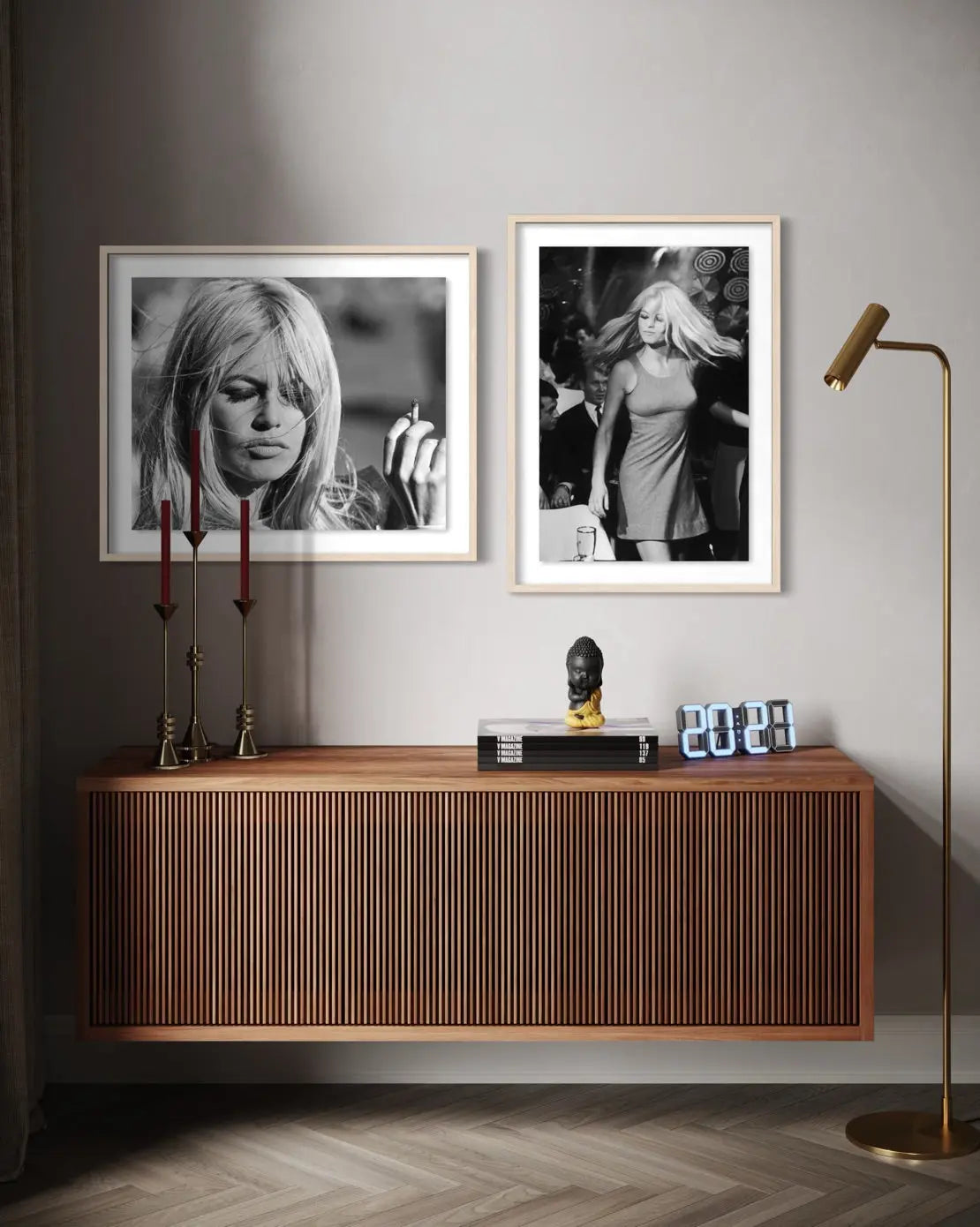 Two framed black and white art prints of iconic blonde women are displayed on a light gray wall above a modern wooden sideboard. The room is styled with a brass floor lamp, decorative candlesticks, and a small bust.