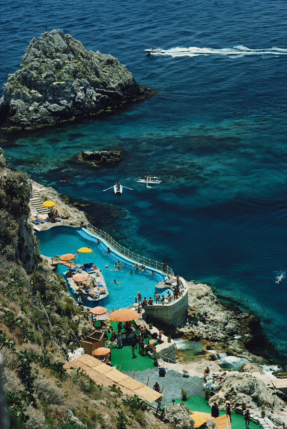 Aerial view of a luxurious pool complex with crystal clear blue water and rocky cliffs. The Picturalist Slim Aarons Collection.  Coastal Photography. 