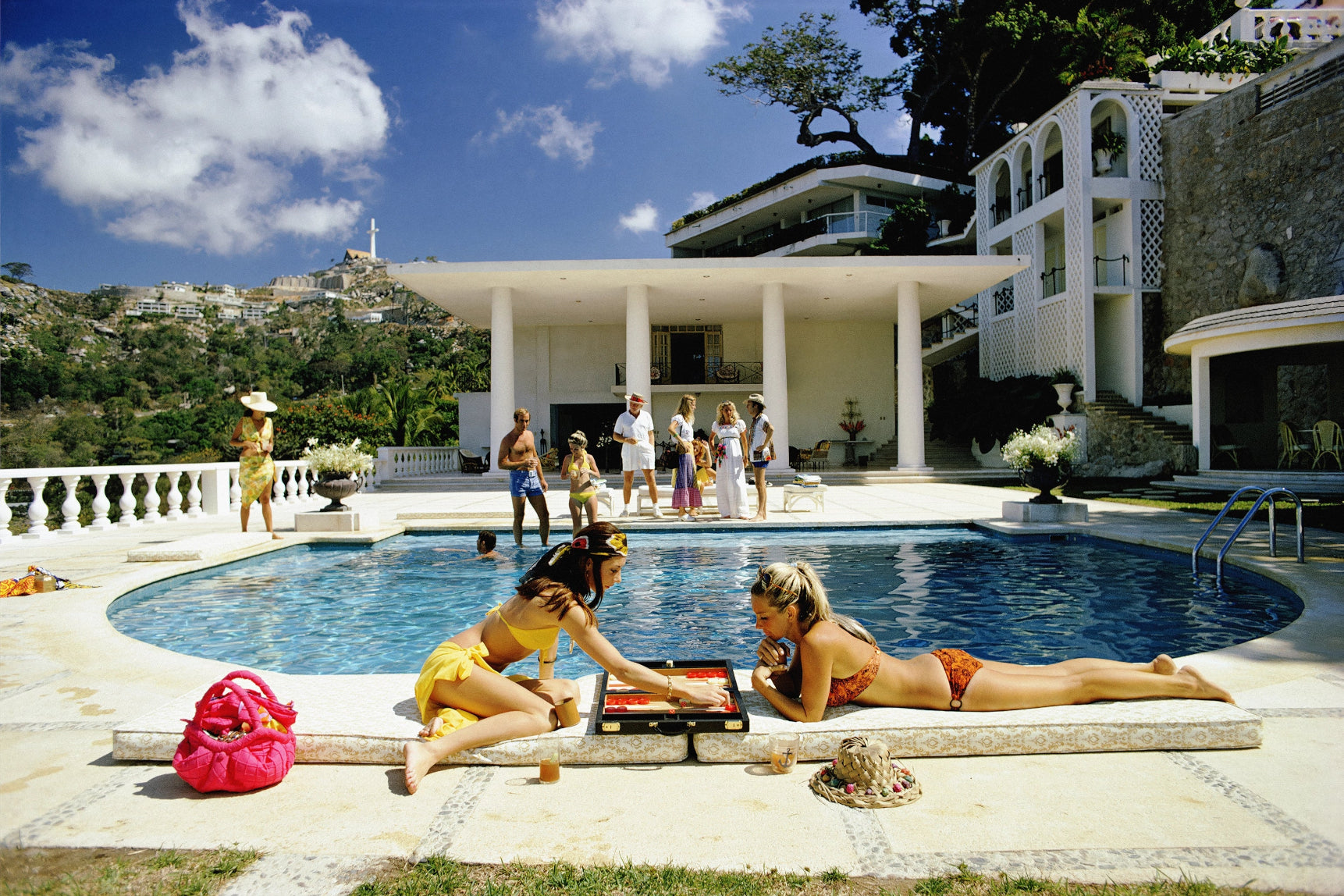 People by a pool with a large house in the background