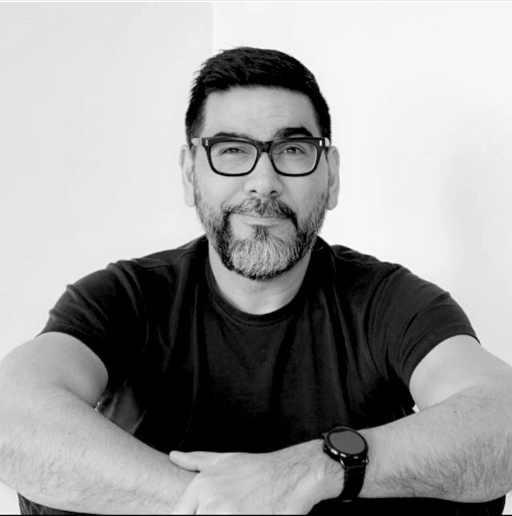 Black and white photo of a man with glasses and a beard wearing a black t-shirt.