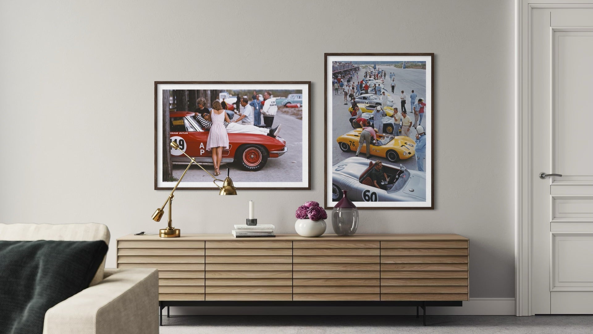 Two framed vintage race car prints displayed side-by-side on a light gray wall above a wooden console table in a modern living room setting.