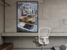 Framed poster of a race car scene on a concrete wall above a chair.