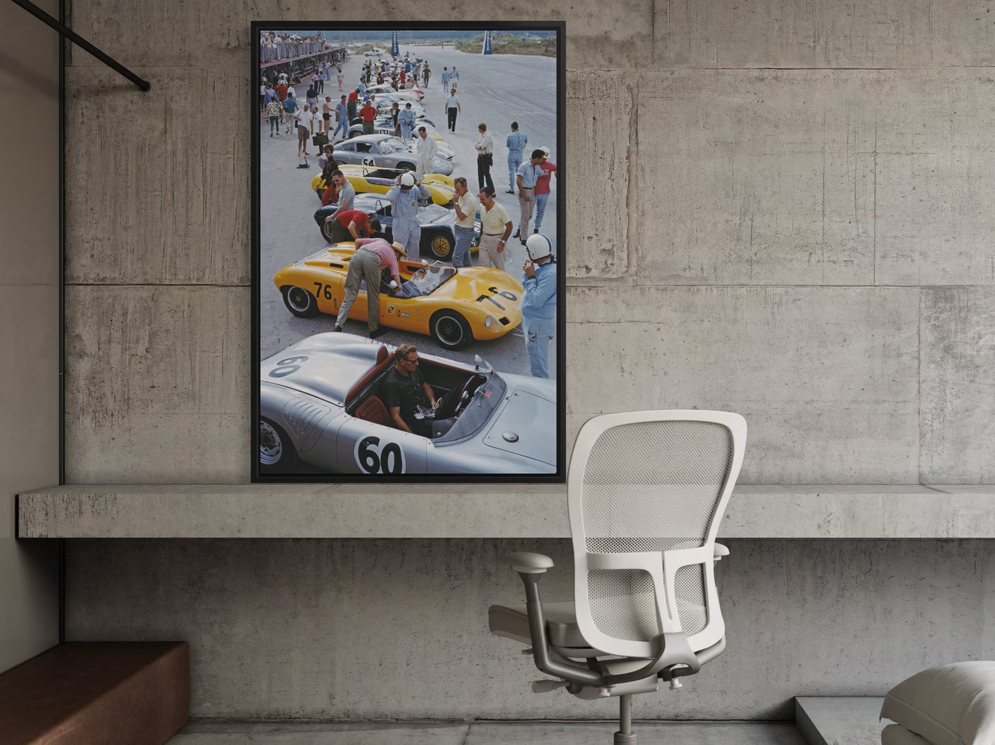 Framed poster of a race car scene on a concrete wall above a chair.