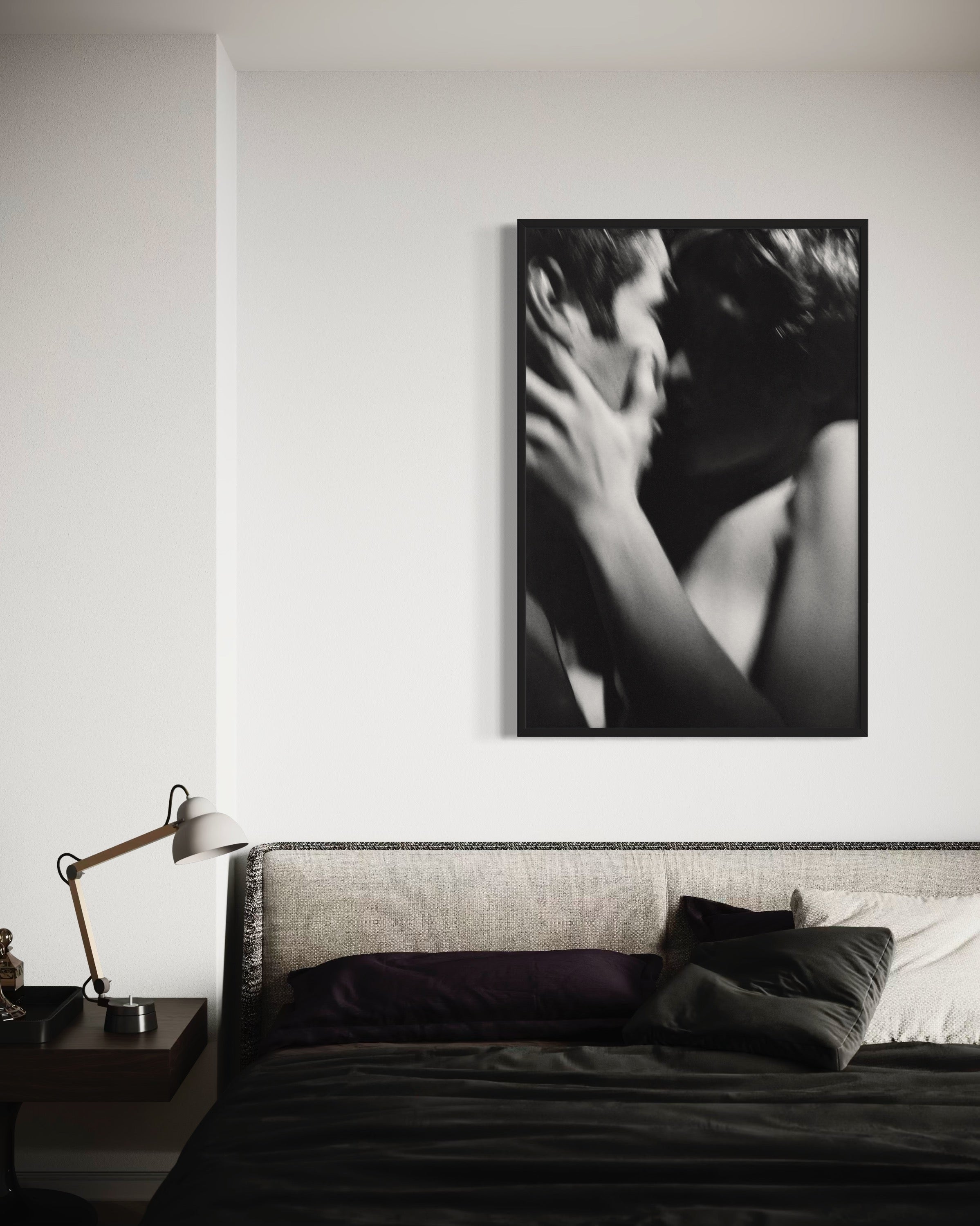 Black and white photograph of a couple embracing on a wall above a bed.