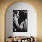 Dining room with a round wooden table and chairs, featuring a black and white painting of two people embracing on the wall.