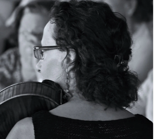 Person with glasses and dark hair, wearing a black top, sitting in an auditorium.