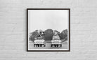 Framed black and white photograph of two children in toy cars on a brick wall.