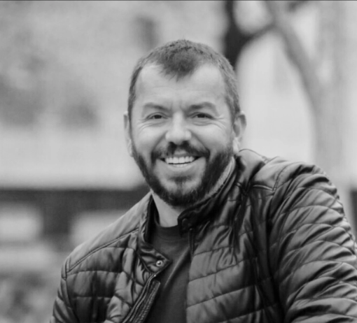 Black and white photo of a man with a beard smiling outdoors