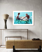 A framed art print depicting a couple sitting at a table over clear turquoise water, displayed on a textured light gray wall above a modern console table and textured bench. The Picturalist Wall Art and Photography. Slim Aarons Collection. Poolside. 