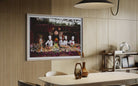 A framed art print depicting chefs preparing food hangs on a light wood slatted wall in a modern dining room setting with a table, chairs, and a pendant light. The Picturalist Wall Art and Photography for Designed Interiors. Slim Aarons Collection, Poolside. Getty Images Gallery. 