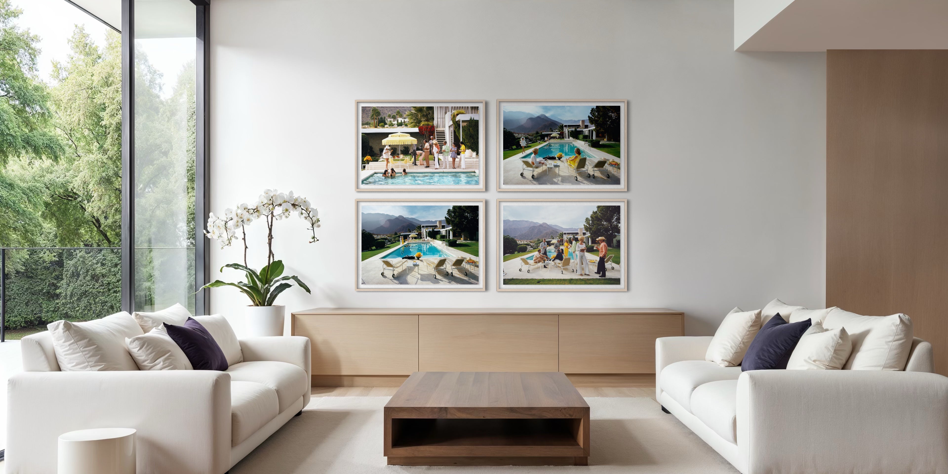 A modern living room with two white sofas and a wooden coffee table, featuring a wall-mounted four-panel framed print set above a low wooden console. The artwork consists of four square color photographs showing poolside scenes with people and outdoor landscapes. The Picturalist Wall Art and Photography for Designed Interiors. Slim Aarons Collection, Poolside. Getty Images Gallery. 