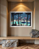 A framed art print depicting a sunny poolside scene with blue water, umbrellas, and tall dark trees, displayed on a beige wall above a wooden bench with decorative rocks.
