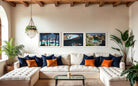 A styled living room featuring a cream tufted sectional sofa with navy and orange accent pillows, a glass coffee table, and three framed landscape photographs on the wall above the couch.
