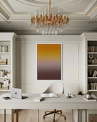 A vertical abstract art print featuring a warm yellow-to-brown gradient, displayed on a white wall in a modern, elegant home office setting with a desk, chair, and chandelier.