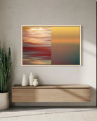 A framed abstract wall art print hangs above a light wood console table in a modern interior. The artwork is split into two vertical sections: the left side shows blurred streaks of red, orange, and gold, while the right side shows a smooth gradient from yellow to teal.