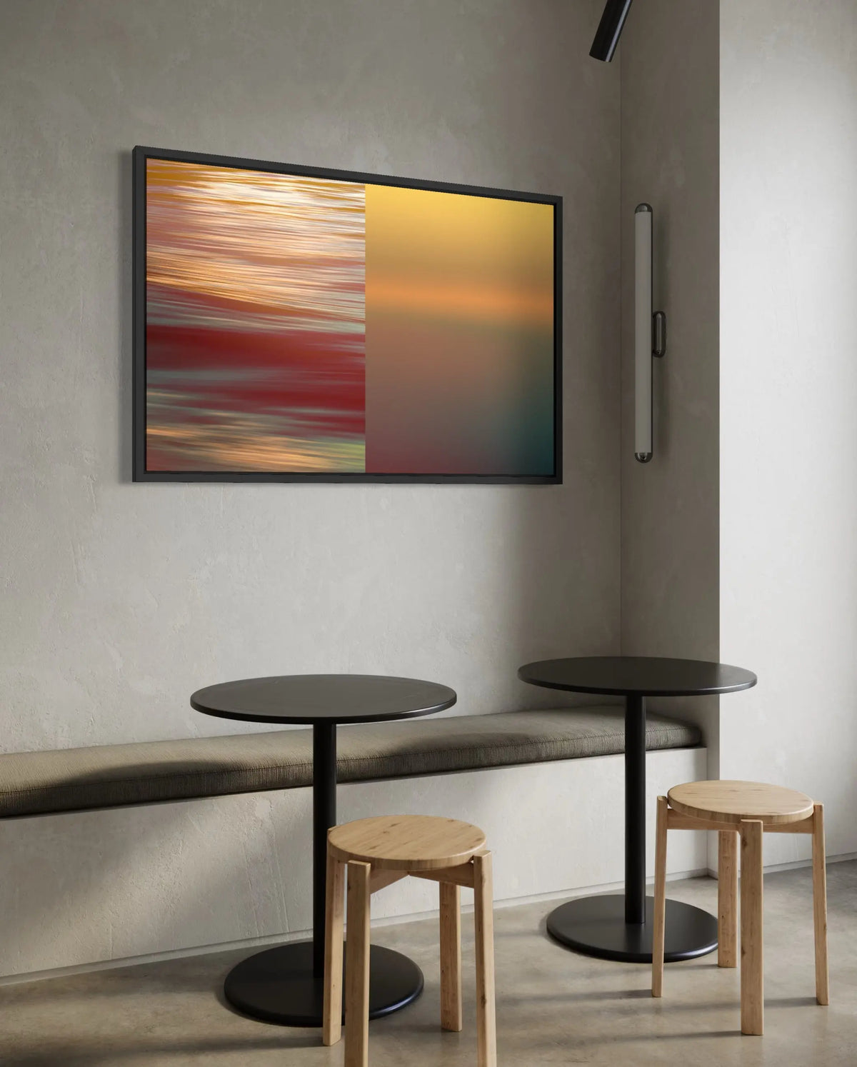 A framed abstract art print featuring a split design of orange, red, and yellow motion-blur on the left, and a smooth yellow-to-teal gradient on the right, displayed on a textured gray wall above a bench and tables.