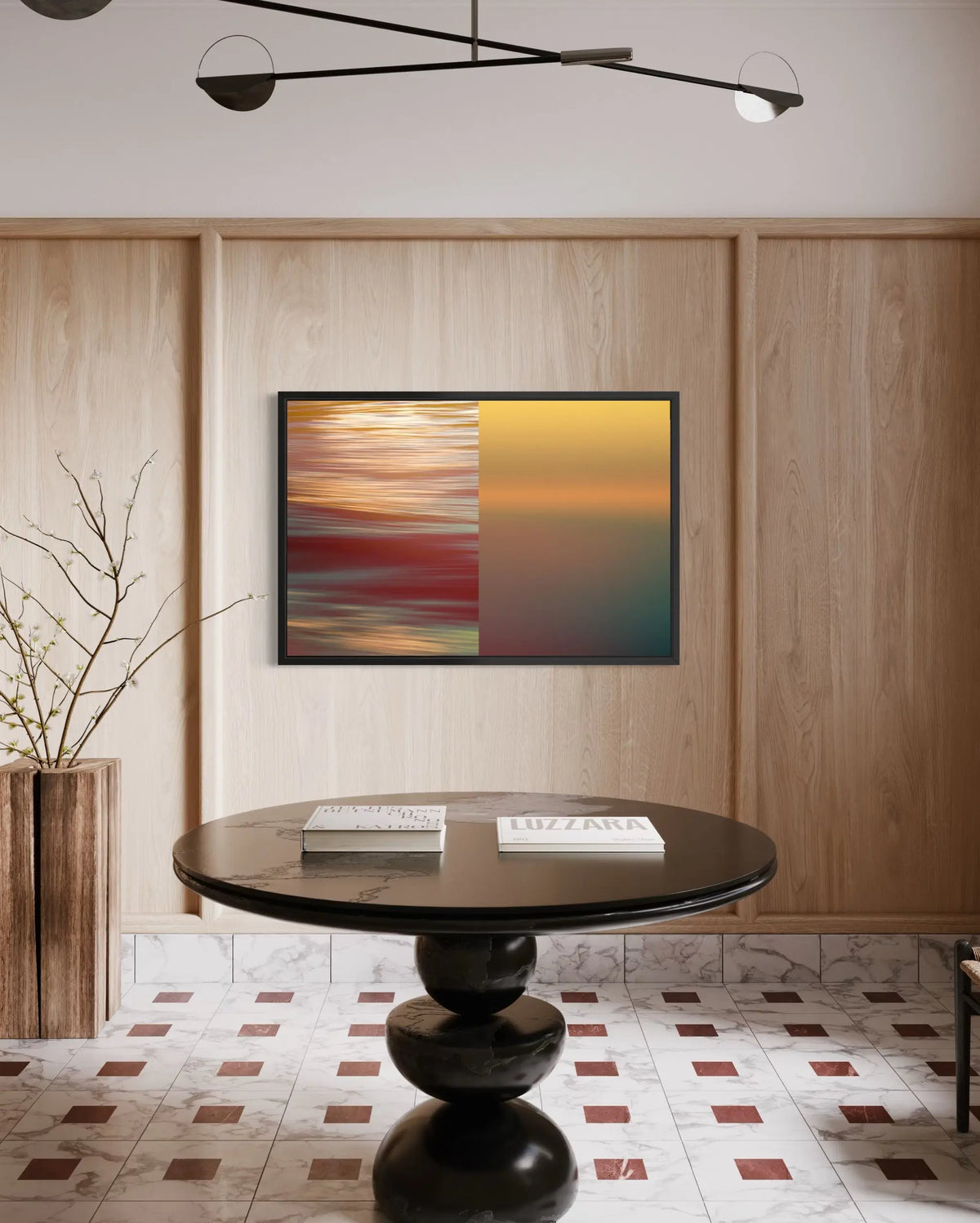 A framed abstract art print hangs on a light wood-paneled wall above a round black table in a modern interior setting.