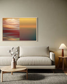 A framed abstract wall art print hangs above a light beige sofa in a styled living room. The artwork is split vertically into two sections: the left side features a blurred red, orange, and teal horizontal pattern, while the right side shows a smooth warm yellow-to-teal gradient.
