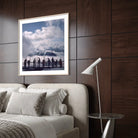 A framed art print depicting a scenic mountain landscape with silhouetted figures under a cloudy sky, styled on a dark wood-paneled wall above a bed in a modern bedroom setting.