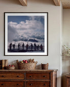 A framed art print depicting a scenic mountain landscape with silhouetted figures, displayed on a beige wall above a rustic wooden dresser in a styled room setting.