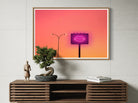 Framed artwork with a pink light bulb on a wooden console table.