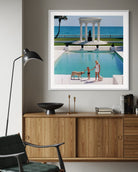 Framed photograph of a pool scene with people and a dog, displayed on a wall above a wooden cabinet.