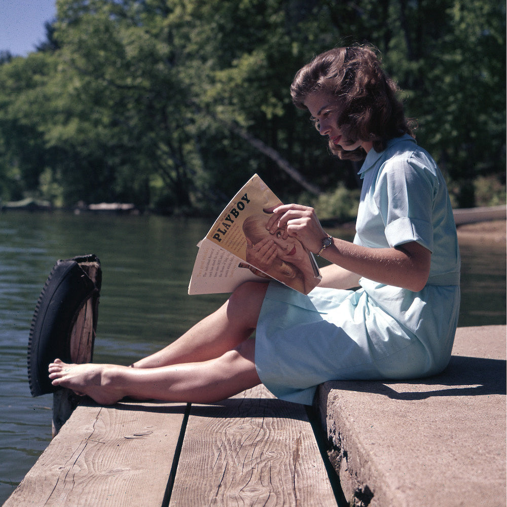 Playful Lakeside vintage photograph of a young woman reading on a wooden dock, fine art print custom framed by The Picturalist.