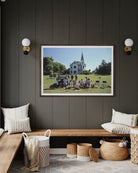 Framed photograph of a group of people on a grassy field with a building in the background, displayed on a dark wall above a wooden bench.